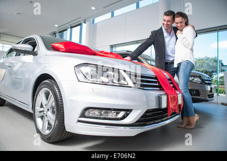 Mann mit Freundin im Autohaus Neuwagen mit roter Schleife zu betrachten Stockfoto