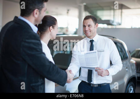 Mitte erwachsenes paar machen Deal mit Verkäufer im Autohaus Stockfoto