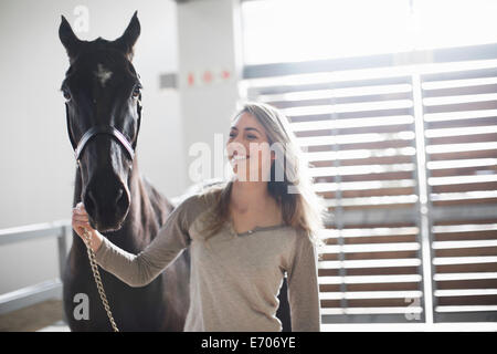 Junge Frau führt schwarzes Pferd im Stall Stockfoto