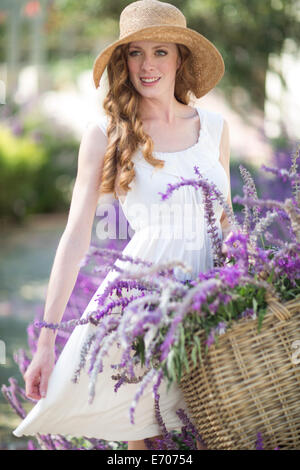 Porträt der schönen jungen Frau im Garten mit Korb mit lila Blumen Stockfoto