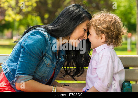 Junge Mutter und Sohn von Angesicht zu Angesicht auf Parkbank Stockfoto