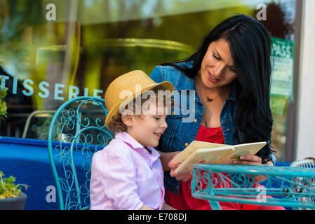 Junge Mutter Geschichte Buch mit Sohn im Straßencafé Stockfoto
