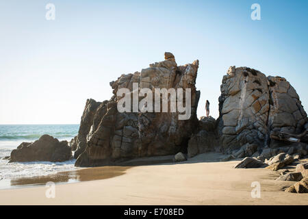 Junge Frau, die auf den Felsen am Strand Stockfoto