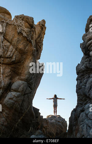 Junge Frau, die auf den Felsen am Strand, ausgestreckten Armen Stockfoto