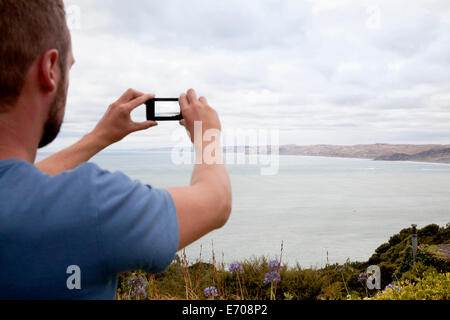 Hinten beschnitten Blick des jungen Mannes fotografieren Meer mit smartphone Stockfoto