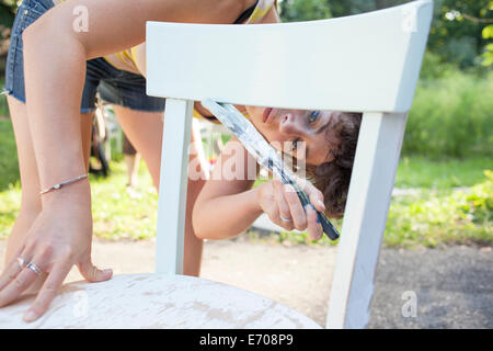 Mitte Erwachsene Frau beugen nach vorne zu malen und wiederherstellen Stuhl im Garten Stockfoto