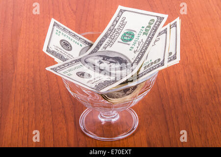 Hundert-Dollar-Banknoten in Glasschüssel auf Holztisch.