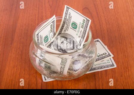 Hundert-Dollar-Banknoten in Glasschüssel auf Holztisch.