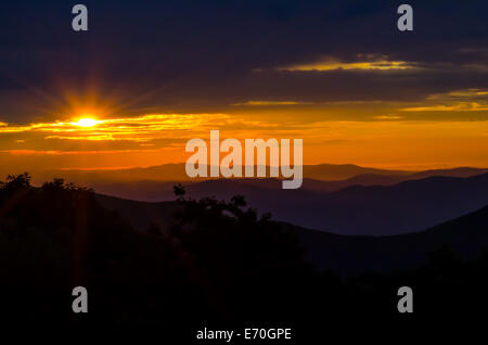 Sonne spähen Sonnenstrahlen durch die Wolken über einem dunstigen lila Bergkette Stockfoto