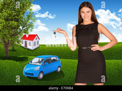 Frau mit Schlüssel in der Hand. Kleines Auto und Haus Gras Stockfoto