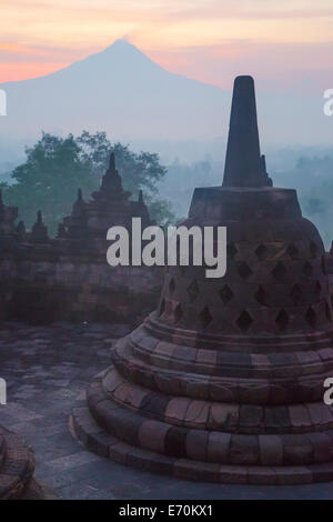 Borobudur, Java, Indonesien.  Stupa und Mount Merapi bei Sonnenaufgang im Morgennebel. Stockfoto