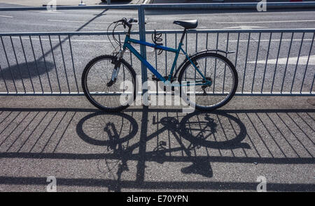 Geparkte Fahrrad gebunden an Zaun Guss Schatten auf Bürgersteig Stockfoto