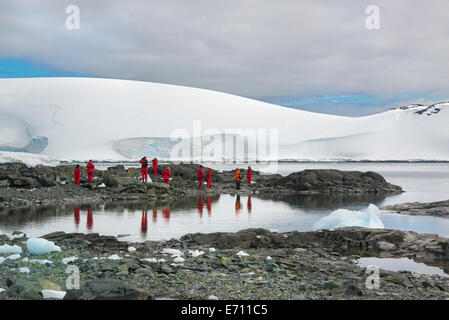 Reisende in hellen orange Regenschutz beobachten und Fotografieren der Landschaft und die Tierwelt auf einer antarktischen Insel. Stockfoto