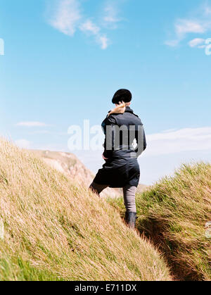 Eine Frau in einem Mantel und Barett ansehen unter den Sanddünen an der Küste. Stockfoto