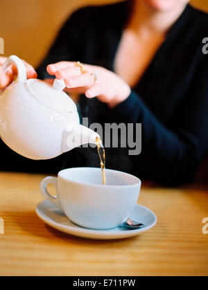 Eine Frau sitzend eine Tasse Tee aus einem Weißware Teekanne gießen. Stockfoto