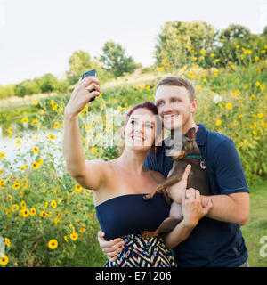 Ein paar spielen mit ihren kleinen Hund in den Park nehmen eine selfy. Stockfoto