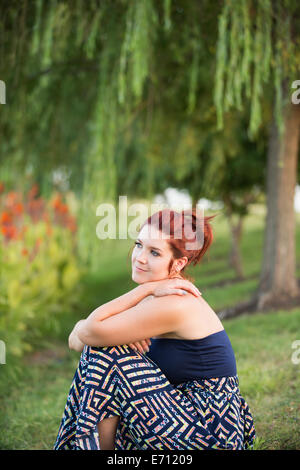Eine Frau sitzt unter einem Baum Trauerweide. Stockfoto
