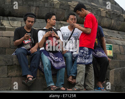 Borobudur, Java, Indonesien.  Junge indonesische Männer überprüfen ihre Handys während des Besuchs des Tempels. Stockfoto