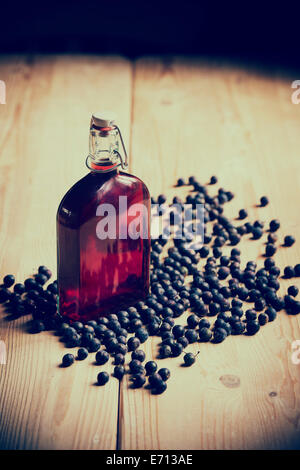 Prunus Spinosa. Blackthorn / Schlehe Beeren und eine Flasche Schlehe gin auf einem hölzernen Küchentisch. Retro-Vintage-Stil Stockfoto