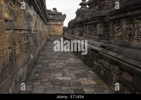 Borobudur, Java, Indonesien. Gehweg um eine Ebene des Tempels. Bas-relief Schnitzereien auf beiden Seiten. Stockfoto
