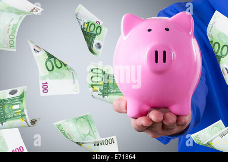 Geschäftsmann Hand mit rosa Sparschwein und hundert Euro-Banknoten auf dunklem Hintergrund fliegen. Stockfoto