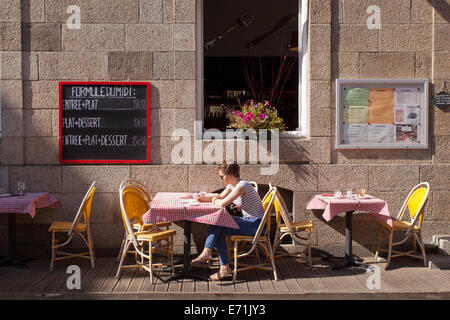 Junge Frau sitzt an einem Tisch vor einem Café in St Malo, Bretagne, Frankreich Stockfoto