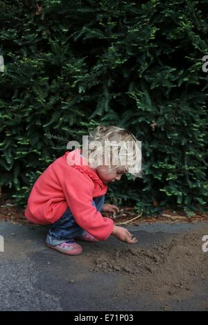 Ein kleines Kind, hocken und mit Schmutz auf dem Boden spielen. Stockfoto