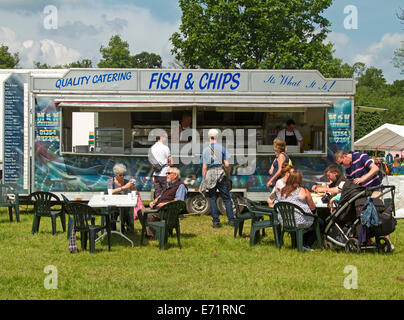 American Diner, darunter Familien mit Kindern, Essen in den Tischen im Freien und Schlange von Kunden an Fish and Chips Stand am Jahrmarkt Stockfoto