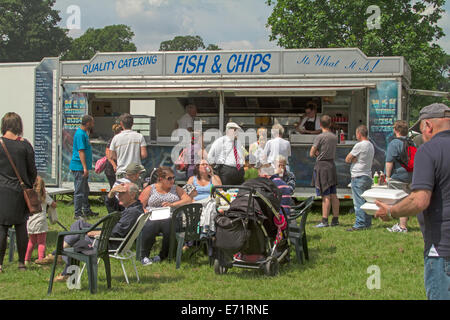 American Diner, darunter Familien mit Kindern, Essen in den Tischen im Freien und Schlange von Kunden an Fish and Chips Stand am Jahrmarkt Stockfoto