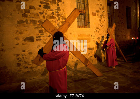 Ein Nazarener trägt ein Kreuz erscheint in einer Wand während der Karwoche in der mittelalterlichen Stadt Cáceres, Extremadura, Spanien Stockfoto