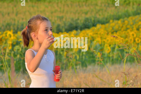 Kleines Mädchen bläst Seifenblasen auf Feld Stockfoto