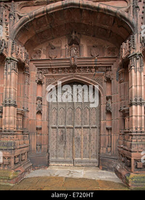 Spektakuläre gewölbte Holztür mit aufwendigen Schnitzereien umgeben von kunstvoll geschnitzten roten Mauerwerk am Eingang zur historischen Chester Kathedrale England Stockfoto