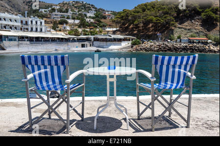 Zwei blaue und weiße Streifen Regiestühle am Kai Wand in Hora Sfakion Sfakia-Kreta Griechenland mit Tavernen im Hintergrund Stockfoto