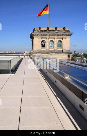 Deutschland, Berlin, deutsche Flagge auf einem Eckturm des Reichstagsgebäudes flattern, wie gesehen von der Dachterrasse mit zwei Touristen schlendern. Stockfoto