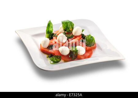 Tomatensalat mit Mozzarella garniert mit Basilikum isoliert auf weißem Teller künstlerisch angeordnet Stockfoto