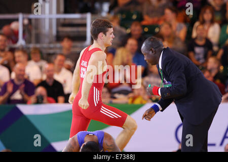 Gareth Jones of Scotland (rot) feiert V Timea Kitiona von Kiribati (blau) in der Mens Freestyle 65 kg Ringen. Stockfoto