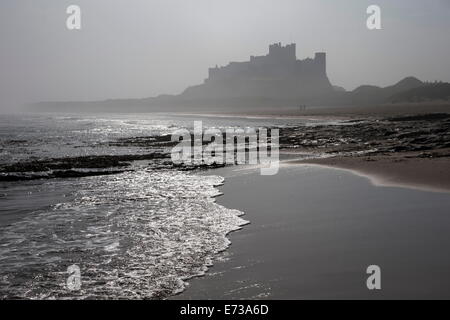 Wellen brechen bei Bamburgh Strand mit Blick auf Bamburgh Castle an einem nebligen Morgen, Northumberland, England, Vereinigtes Königreich Stockfoto