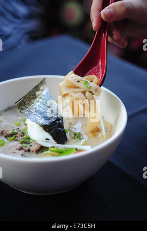 Essen Restaurant asiatische japanische Ramen Nudelsuppe mit einem Spiegelei Hand rot Löffel Stockfoto