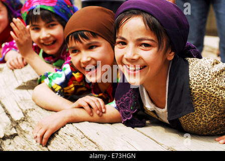 Tadschikistan, Penjakent, Gruppe von einheimischen Mädchen in traditioneller Tracht posiert und spielt am Fluss auf Holzbrücke. Stockfoto