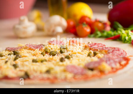 rohe italienische Salami Pizza am Tisch mit Zutaten Stockfoto