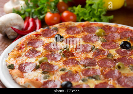 Italienische Salami Pizza am Tisch mit Gemüse Stockfoto