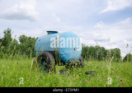 Blaues Wasserzisterne für Tier Stand zwischen hohen Weidegras und Kleeblätter in Wind bewegen. Stockfoto