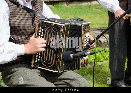 Akkordeonist junger Mann in traditioneller Kleidung spielen Volksmusik mit Akkordeon in ländlichen Partei. Stockfoto