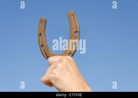 weibliche Hand halten altes rostiges Eisen Hufeisen auf blauen Himmelshintergrund, Symbol für Glück Glück Stockfoto