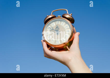 Antike Bronze Uhr mit römischen Ziffern in die Hand der Frau auf blauen Himmelshintergrund Stockfoto