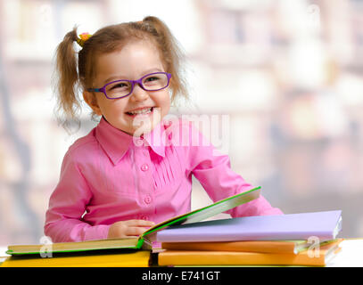 Glückliches Kind Mädchen in Brille lesen von Büchern, die am Tisch sitzen