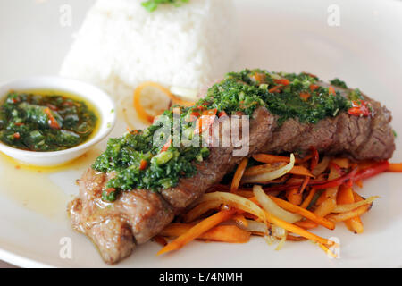 Fleisch mit Chimichurri serviert auf einem Bett aus Gemüse und Reis in einem Restaurant. Stockfoto