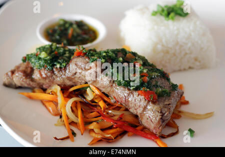 Fleisch mit Chimichurri serviert auf einem Bett aus Gemüse und Reis in einem Restaurant. Stockfoto