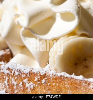 Frische "Brüsseler Waffel" garniert mit Schlagsahne, in Scheiben geschnittene Bananen und Zucker des Konditors, ein beliebtes Gericht in Belgien. Stockfoto