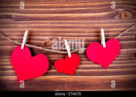 Drei rote Herzen in verschiedenen Größen an einer Linie auf hölzernen Hintergrund hängen Stockfoto